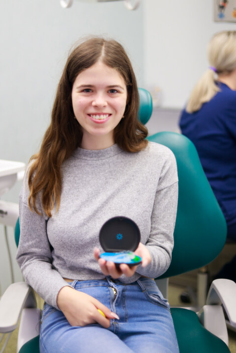 A happy young Park Lane Orthodontics patient holding her clear aligner case